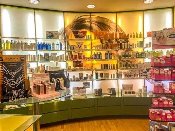 Vetrina di un negozio di cosmetici ben illuminata, con scaffali pieni di profumi e trucchi su banconi verdi curvi.
