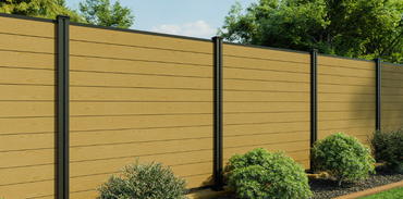 Tan wooden privacy fence with dark posts and green shrubs along the base outdoors