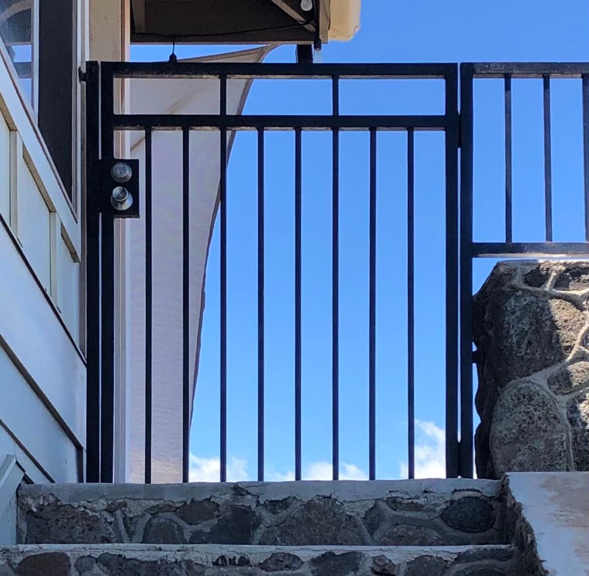 Black metal gate on stone steps against a blue sky.