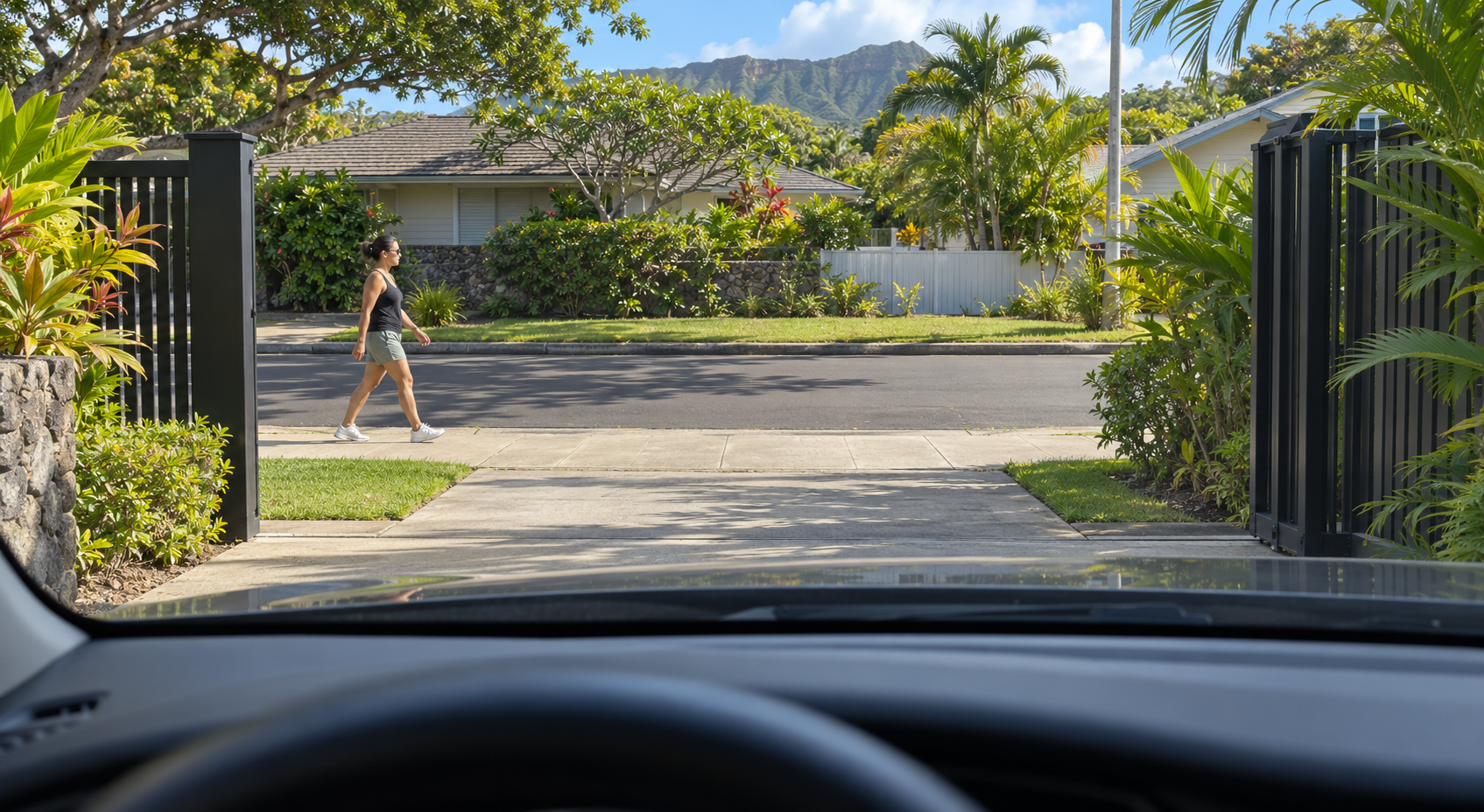 A driver’s-seat view through an open driveway gate shows a pedestrian approaching along the sidewalk