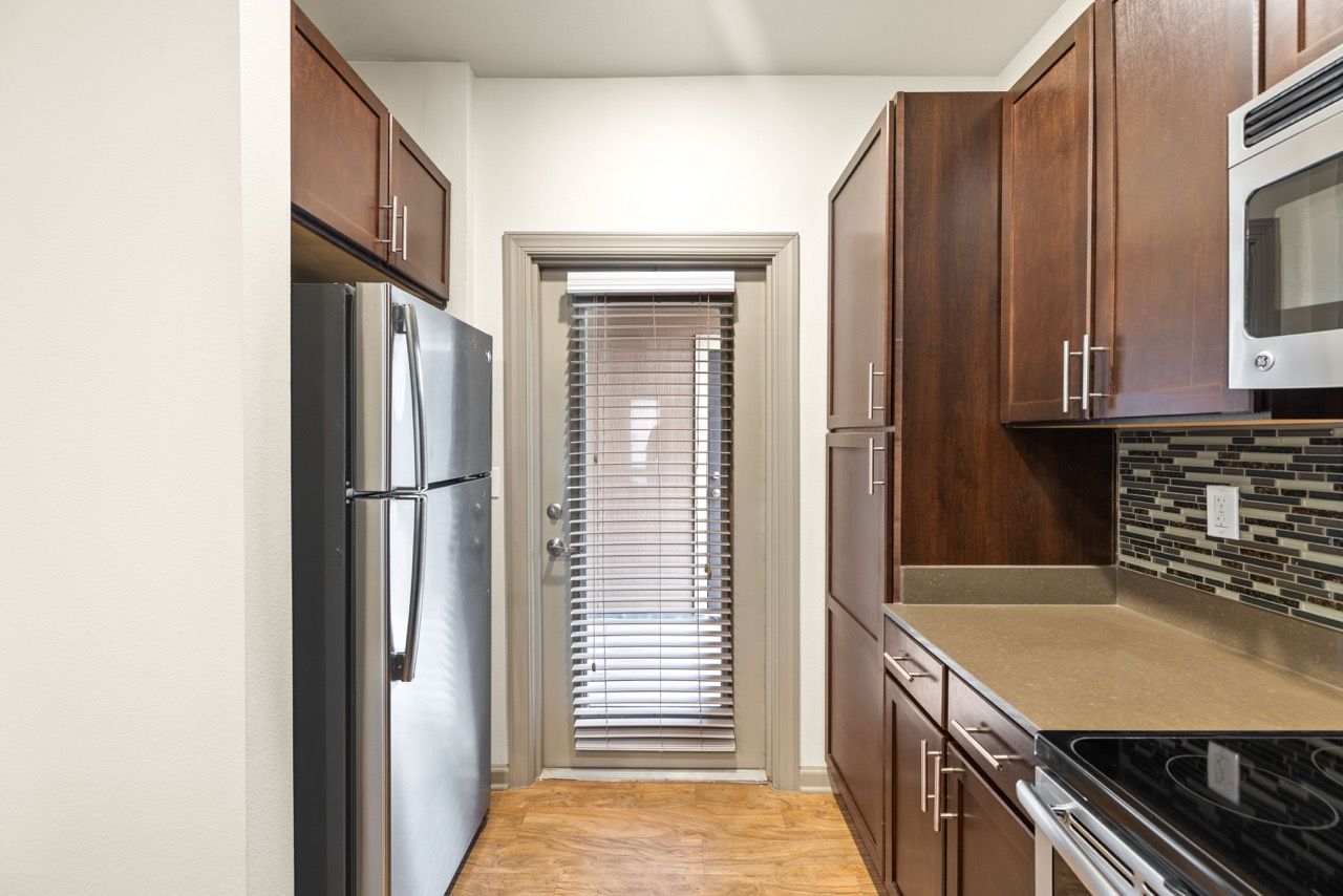 Apartment kitchen with stainless steel refrigerator, dark wood cabinets, and a tile backsplash.