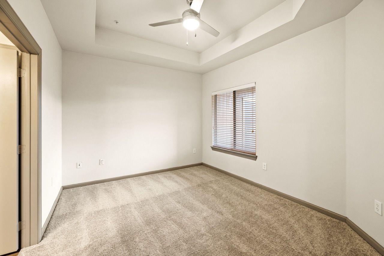 Empty carpeted bedroom with a window, blinds, and a ceiling fan.