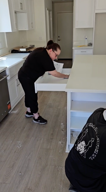 Person in black shirt cleaning a white kitchen counter in a bright, modern kitchen.