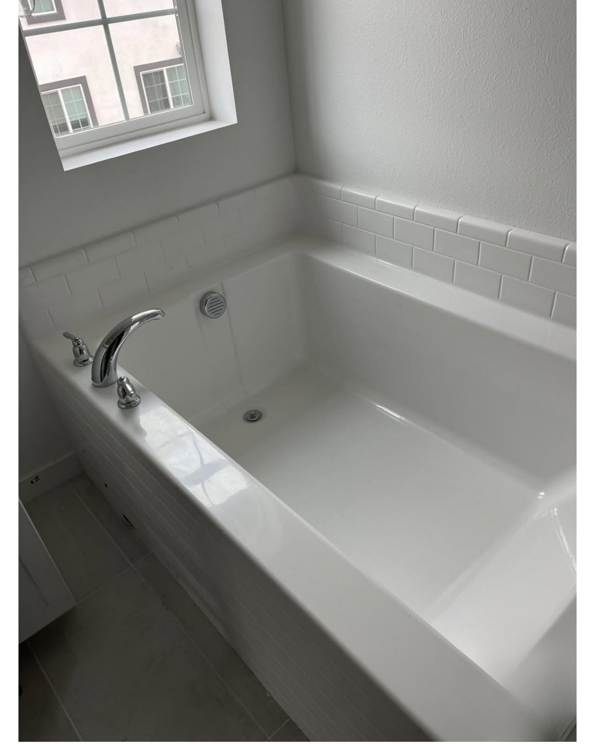 White bathtub with chrome faucet and tiled surround in a bright bathroom near a window