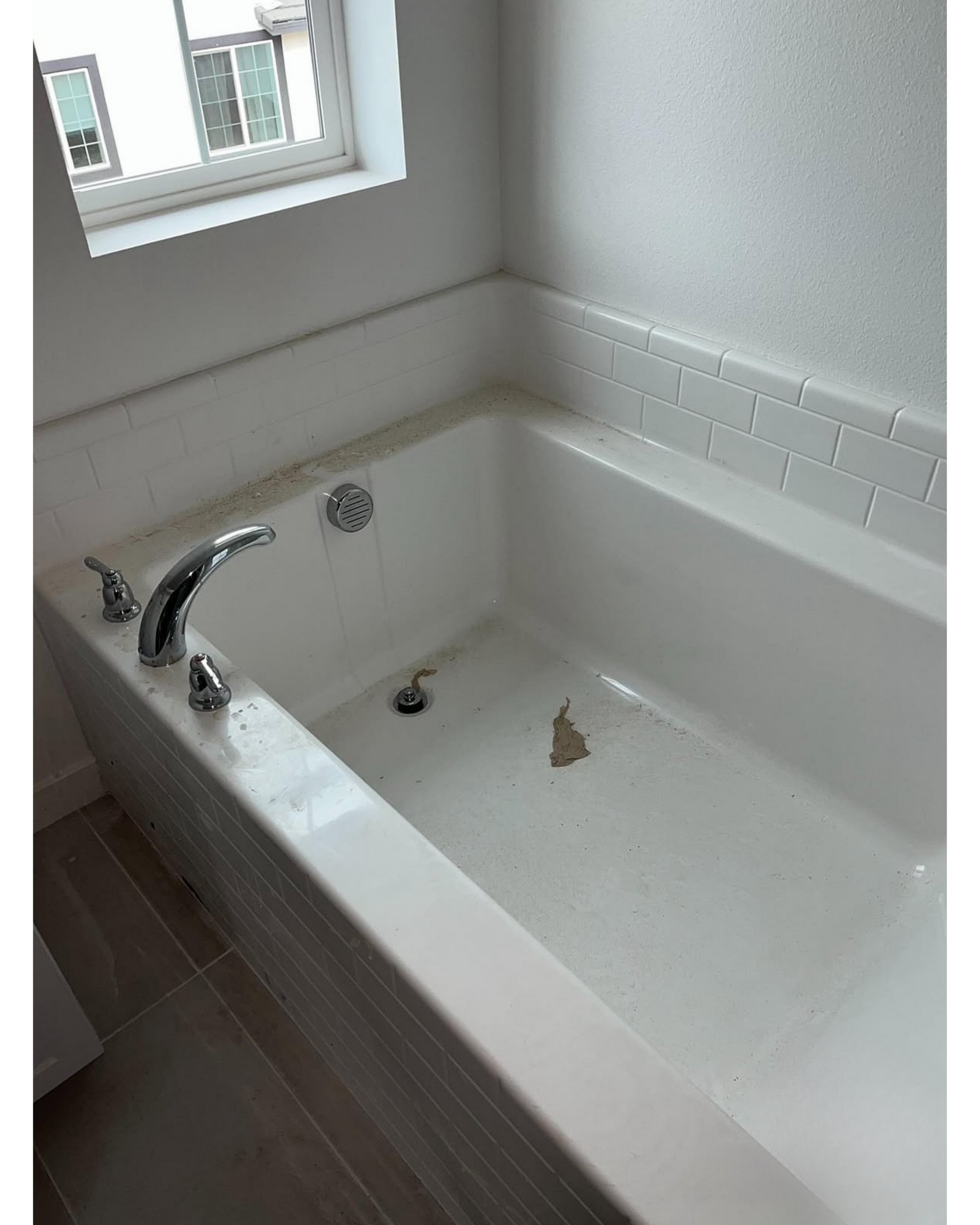 White bathtub with chrome faucet in a tiled bathroom, beside a window.