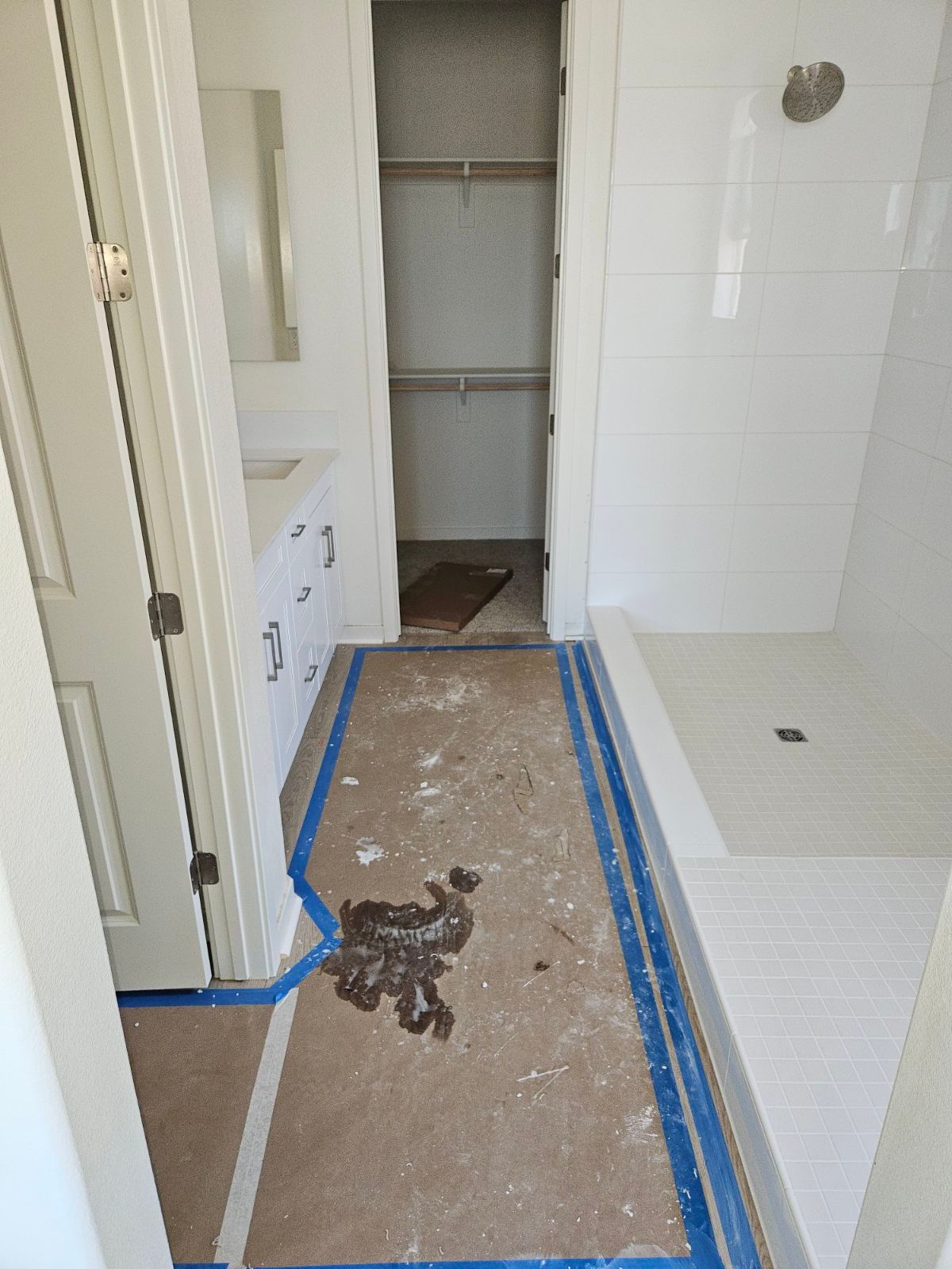 Bathroom under renovation with taped floor protection and debris on the floor.