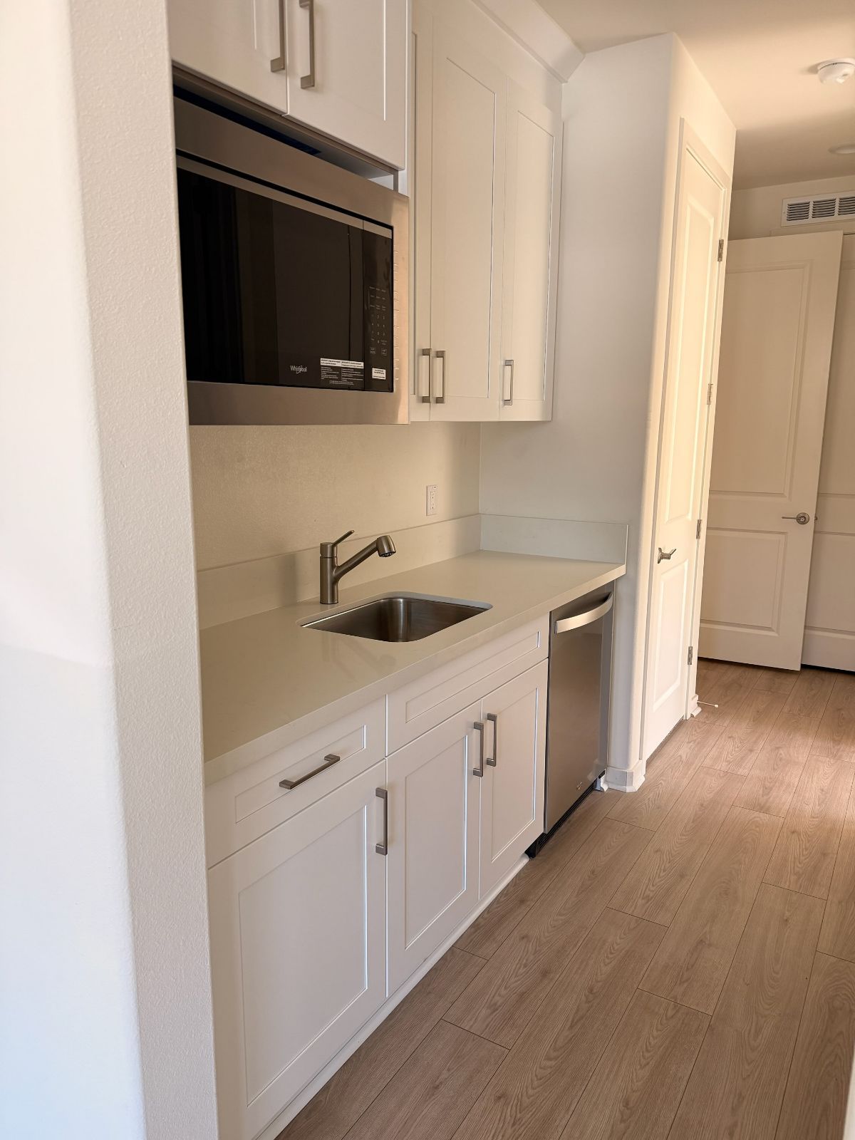 Compact white kitchen with built-in microwave, sink, cabinets, and wood flooring.