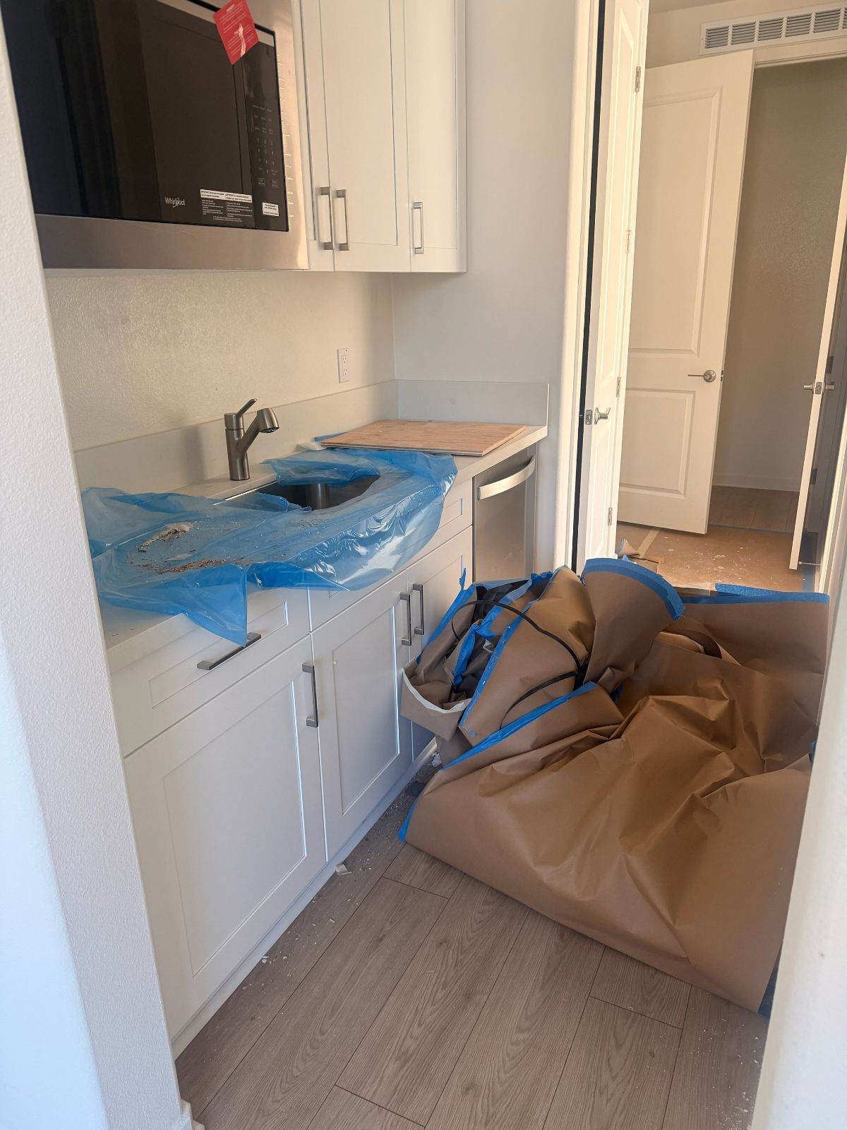 Damaged kitchen with blue-covered countertop, sink, and a large cardboard debris pile on the floor