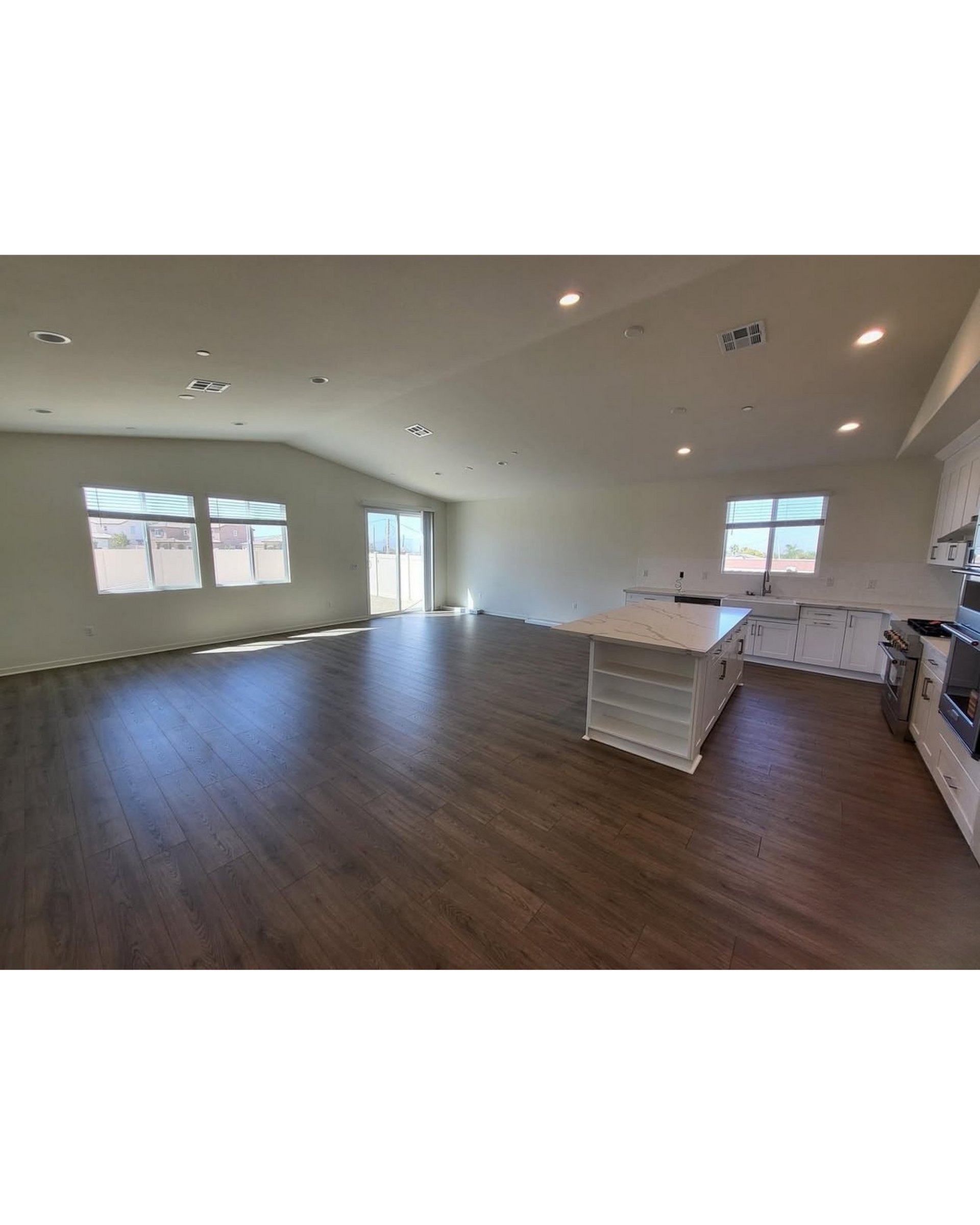 Empty modern living room with dark wood floors, white walls, recessed lights, and large windows.