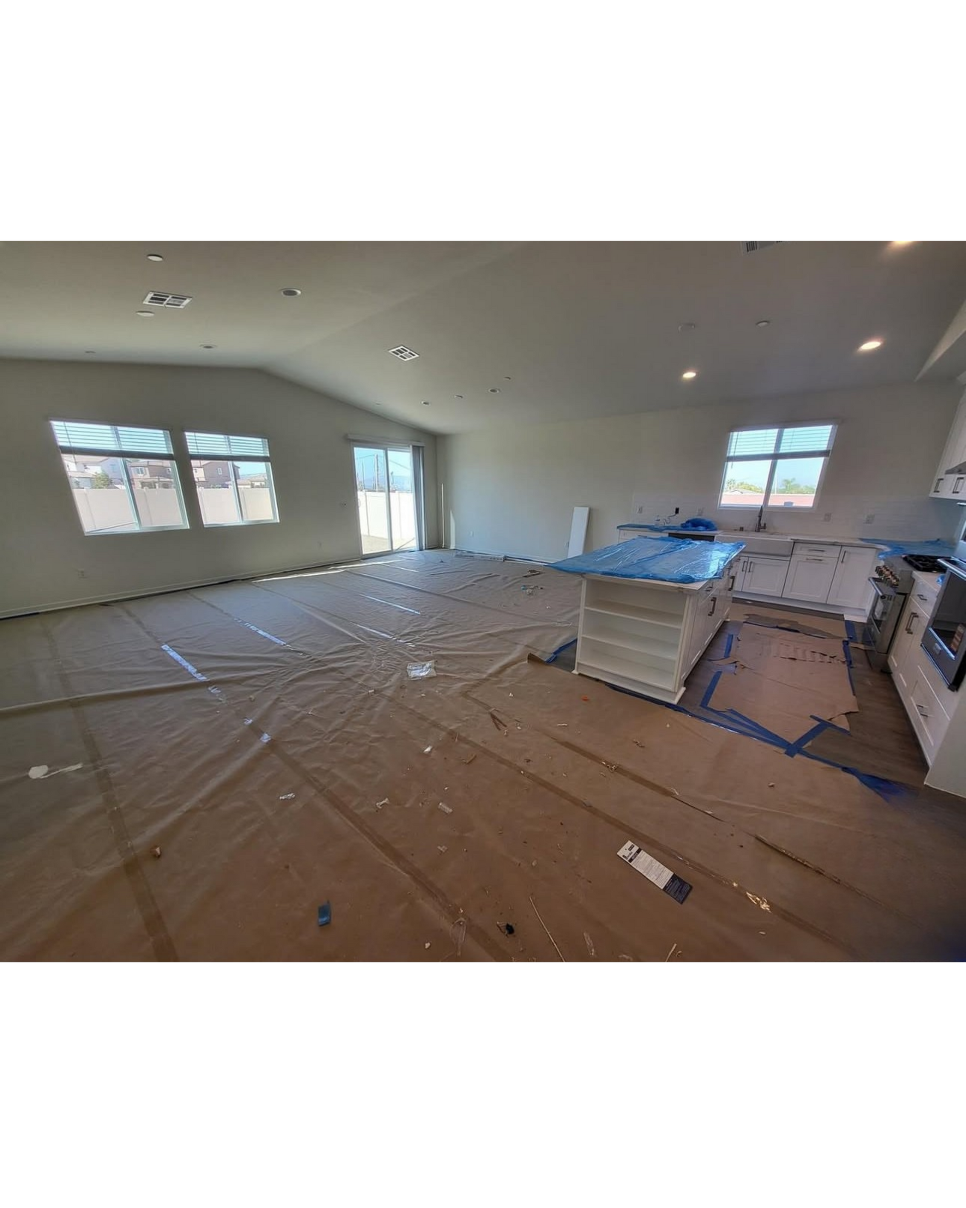 Unfinished room with plastic-covered floor, white walls, windows, recessed lights, and stacked materials