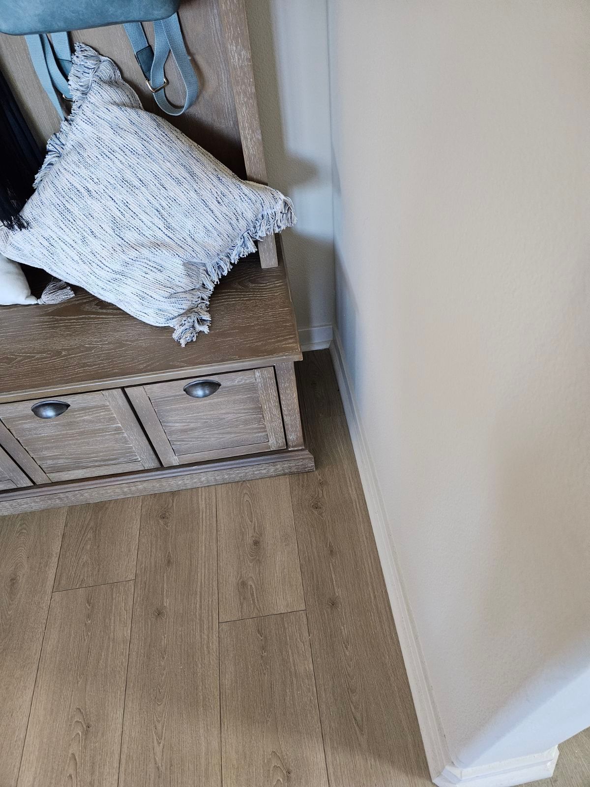 White textured pillow on a wooden bench beside a beige wall and wood floor.