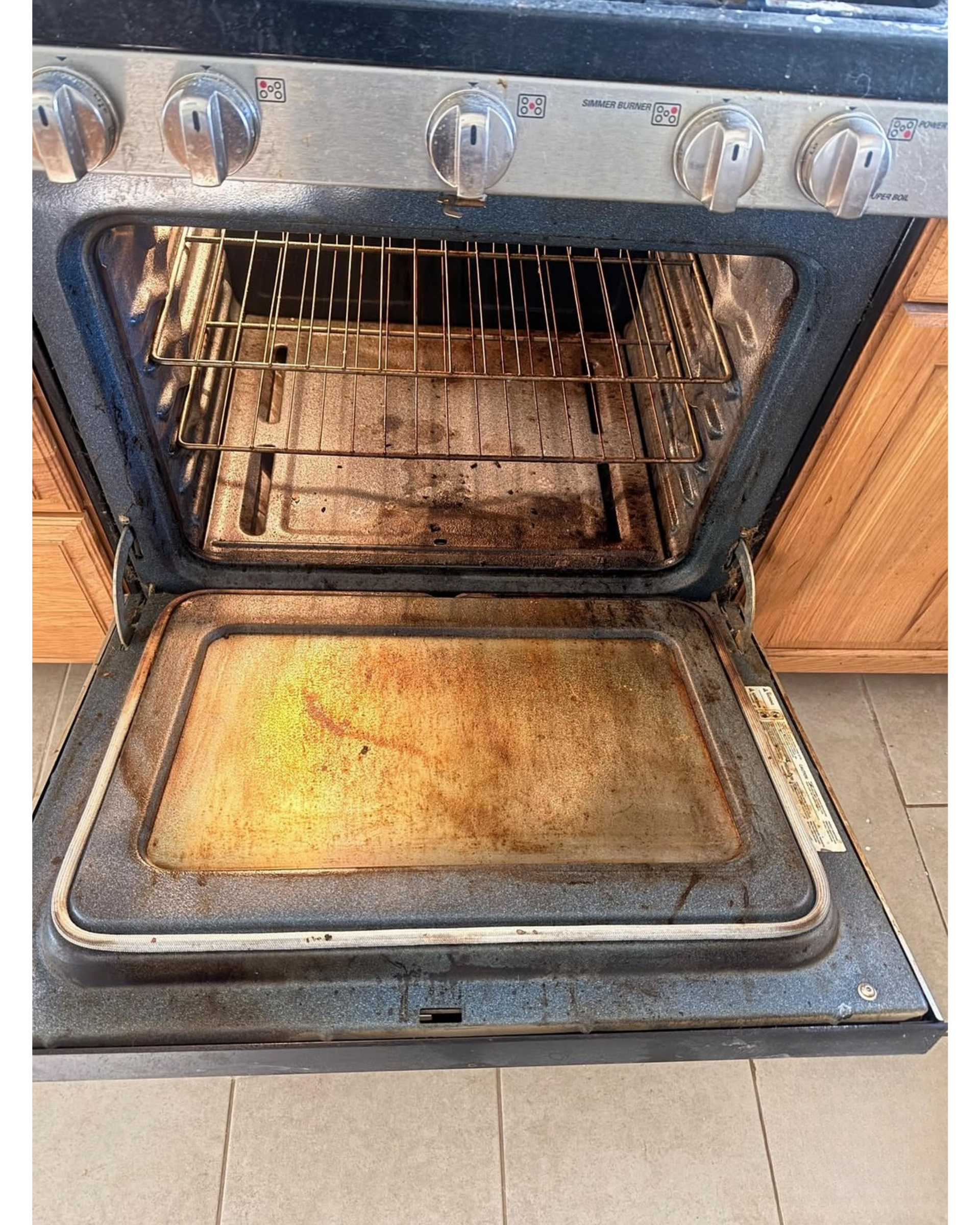 Open dirty oven with stained door and grates in a kitchen