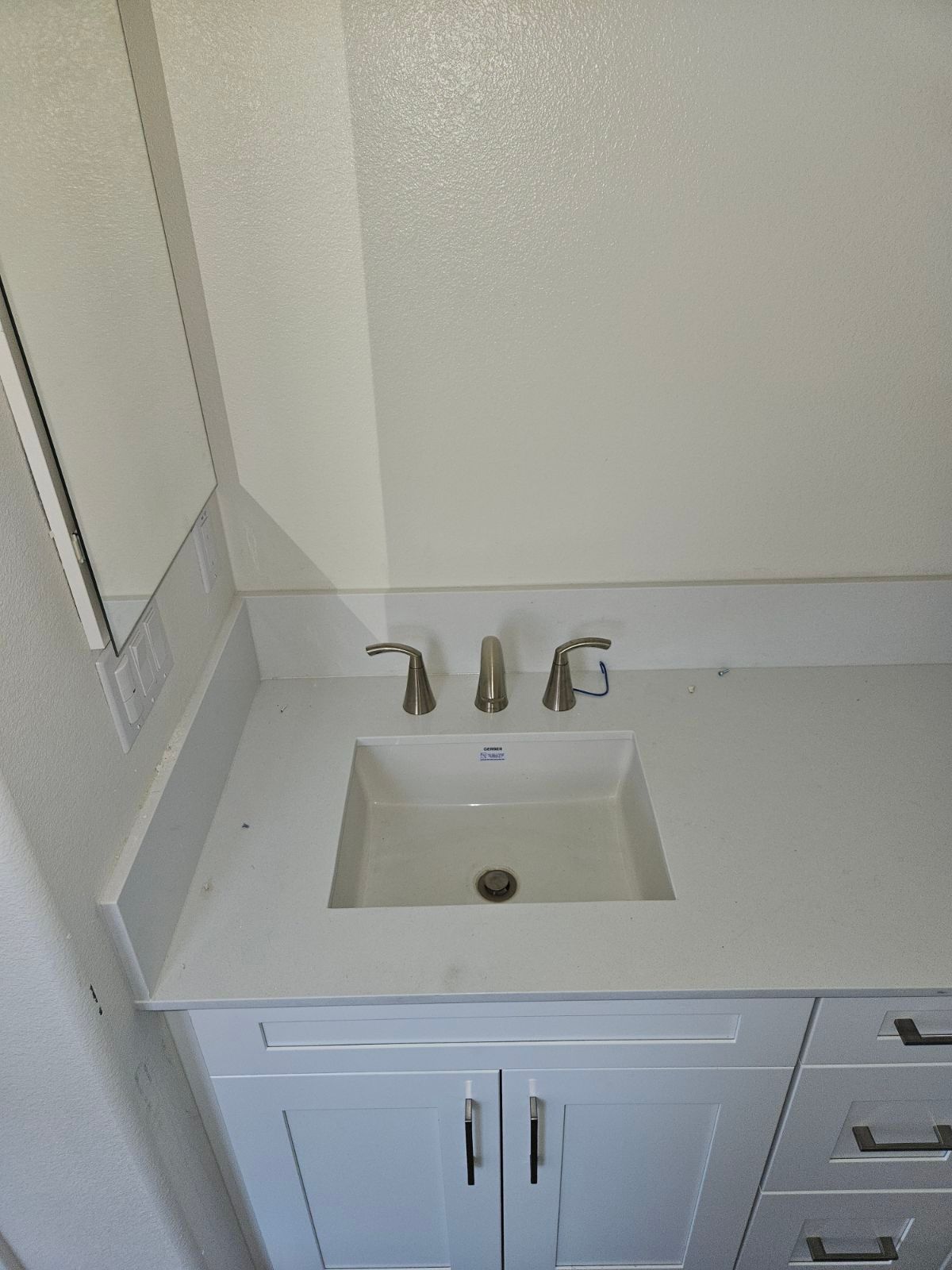 Small bathroom vanity with white countertop, sink, chrome faucet, and cabinet drawers.