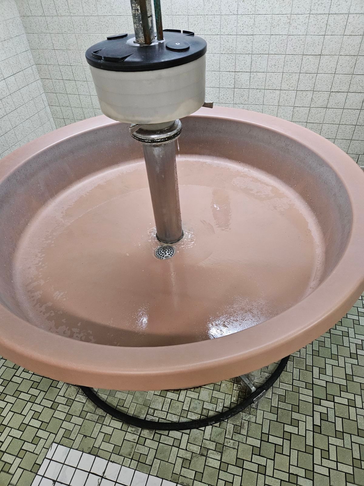 Round pink ceramic sink with a metal faucet in a tiled restroom