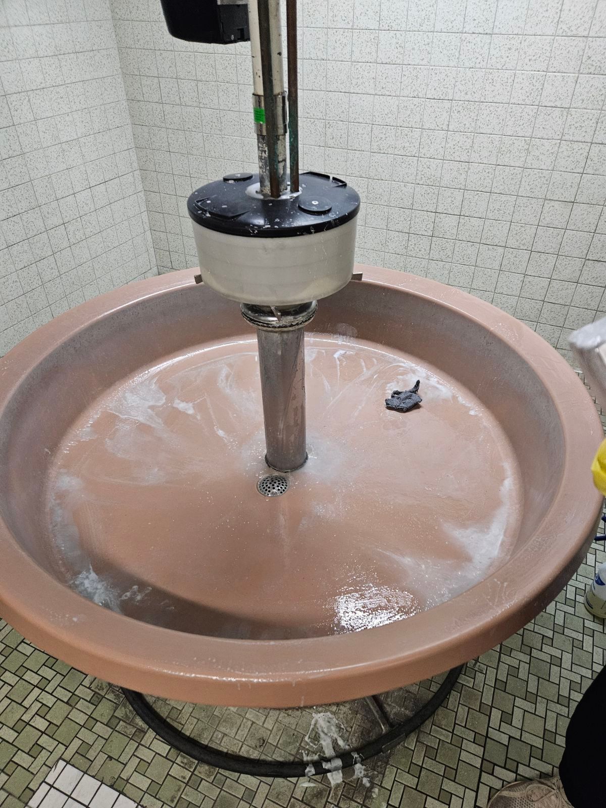 A large peach-colored fountain basin with water flowing from a central column in a tiled room