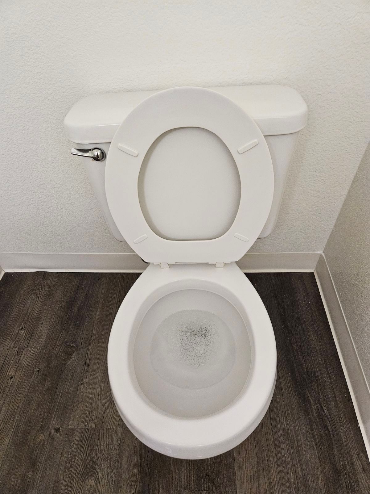 White toilet with seat up in a small bathroom with dark wood flooring.