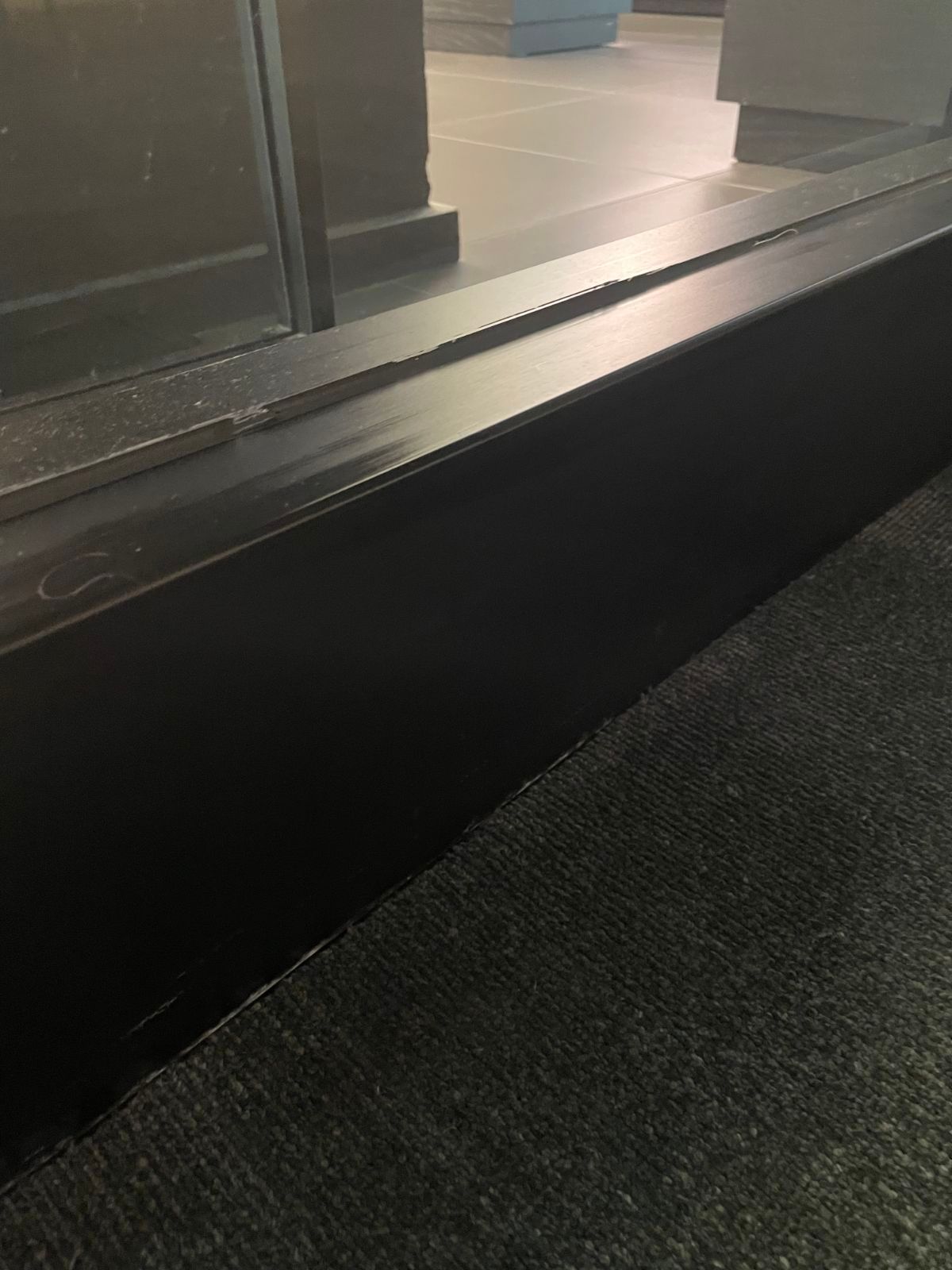 Black metal step/threshold beside a glass door, with a dark floor in the foreground.