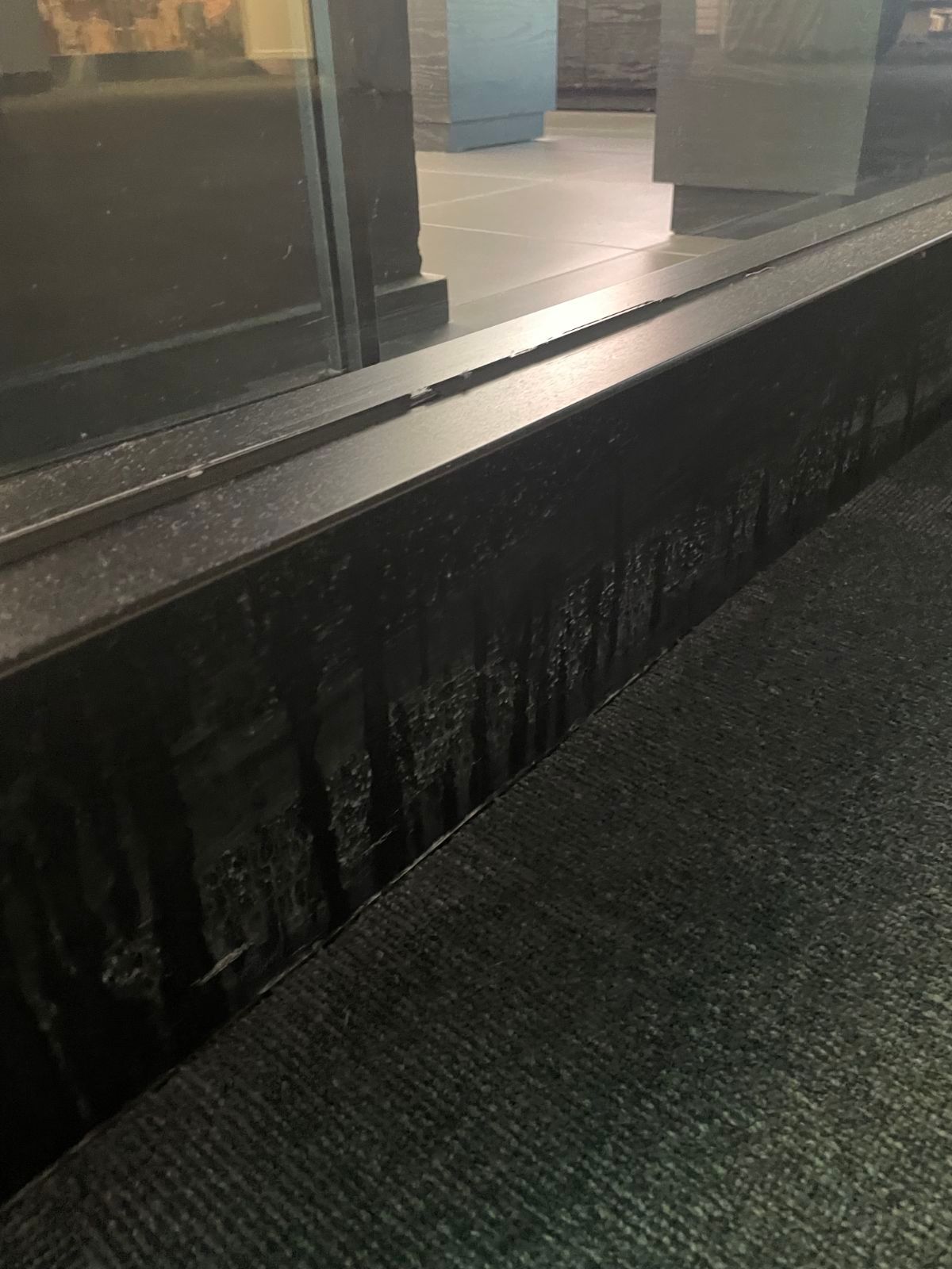 Wet black window ledge beside a glass storefront reflecting light at night