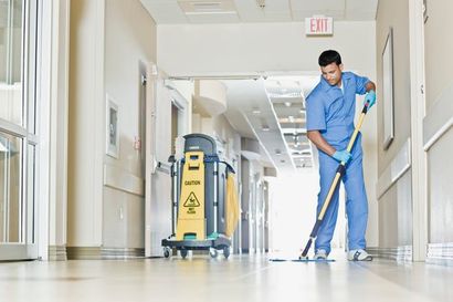 Janitor mopping a hospital hallway beside a cleaning cart