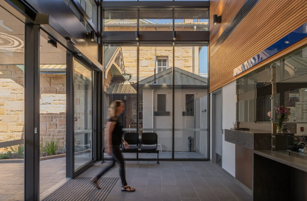 Person walking through a modern glass entryway with a couch inside and wood-paneled walls