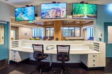 Reception desk with two chairs and four wall-mounted monitors showing nature scenes