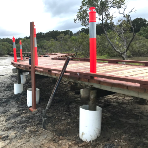 Raised wooden walkway under construction with red safety posts in a wooded area