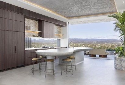 Modern kitchen with a curved island, stools, and open view of mountains through wide windows