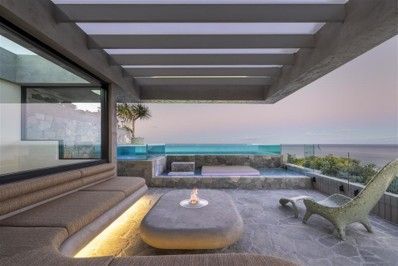 Modern rooftop patio with lounge seating, a fire pit, and an ocean view at sunset