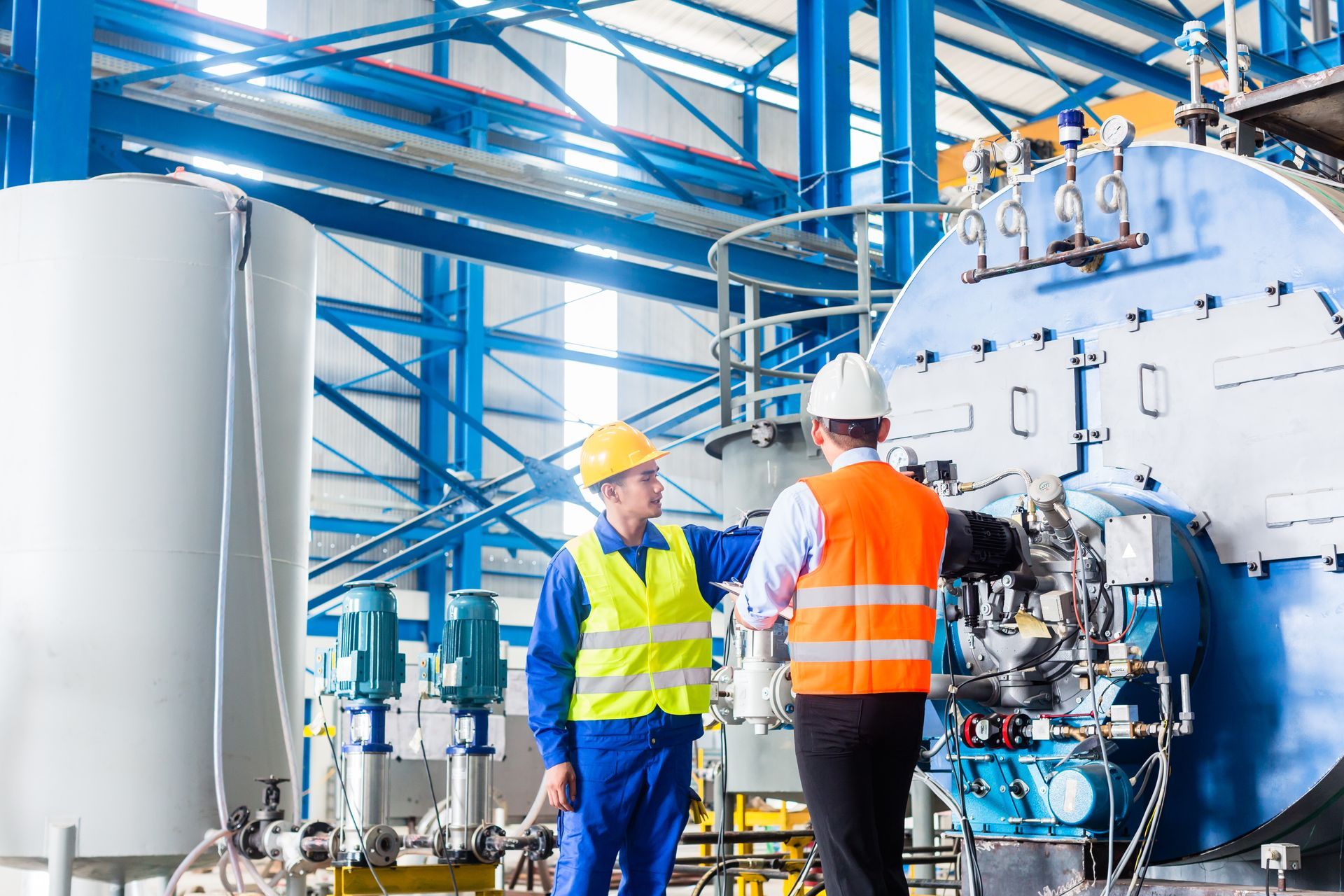 Two workers in safety gear inspect industrial machinery in a factory. Two workers in safety gear inspect industrial machinery in a factory.