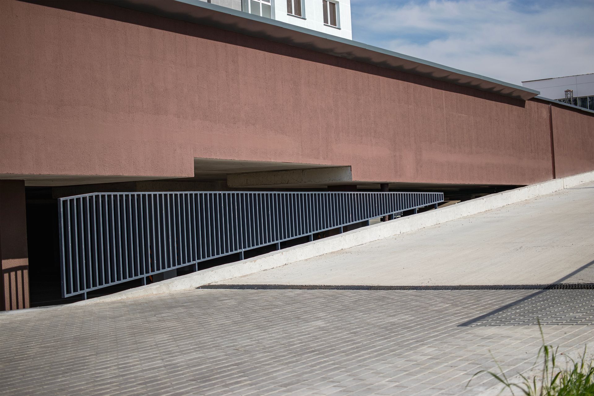 Modern building entrance with a sloped white ramp and black railing beside a brick wall.