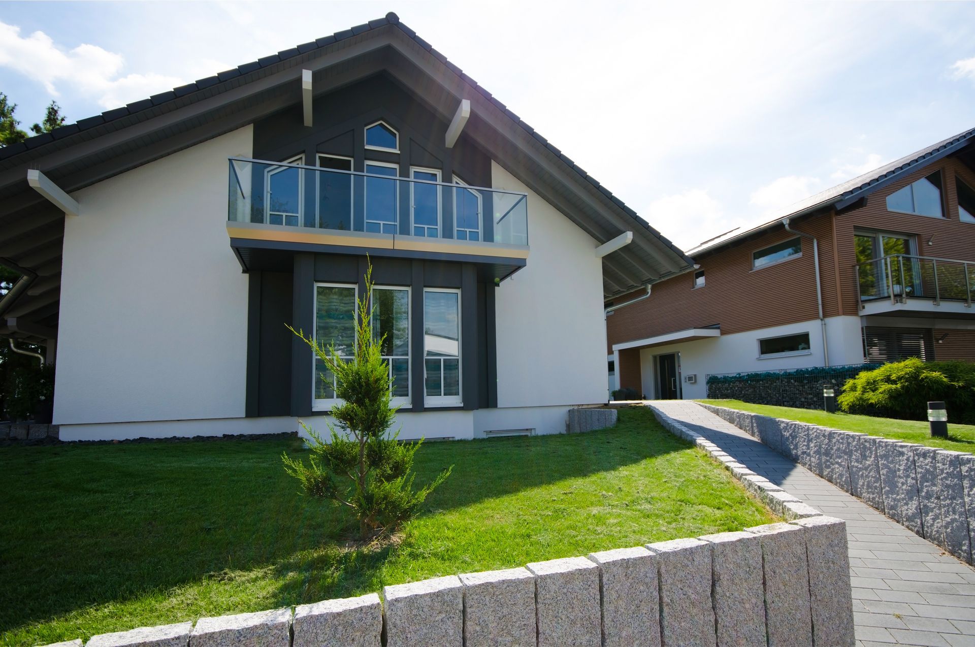 Modern house with white facade, blue balcony, and sloped lawn in front