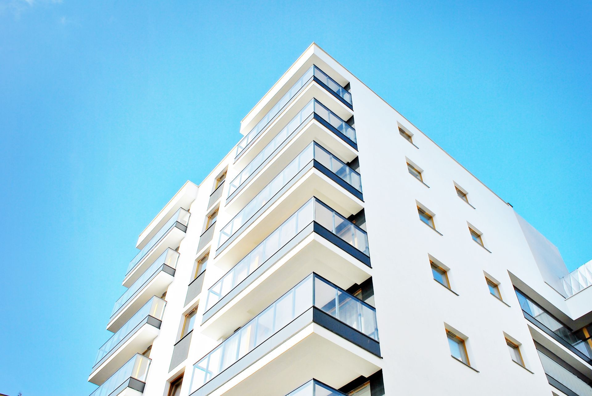 Modern white apartment building viewed from below against a bright blue sky Modern white apartment building viewed from below against a bright blue sky