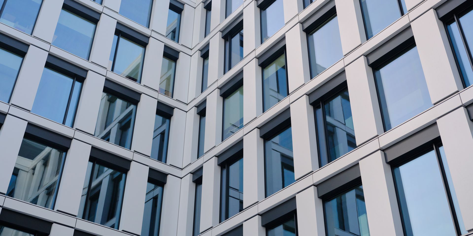 Modern glass office building facade with blue-tinted windows and gray structural beams Modern glass office building facade with blue-tinted windows and gray structural beams