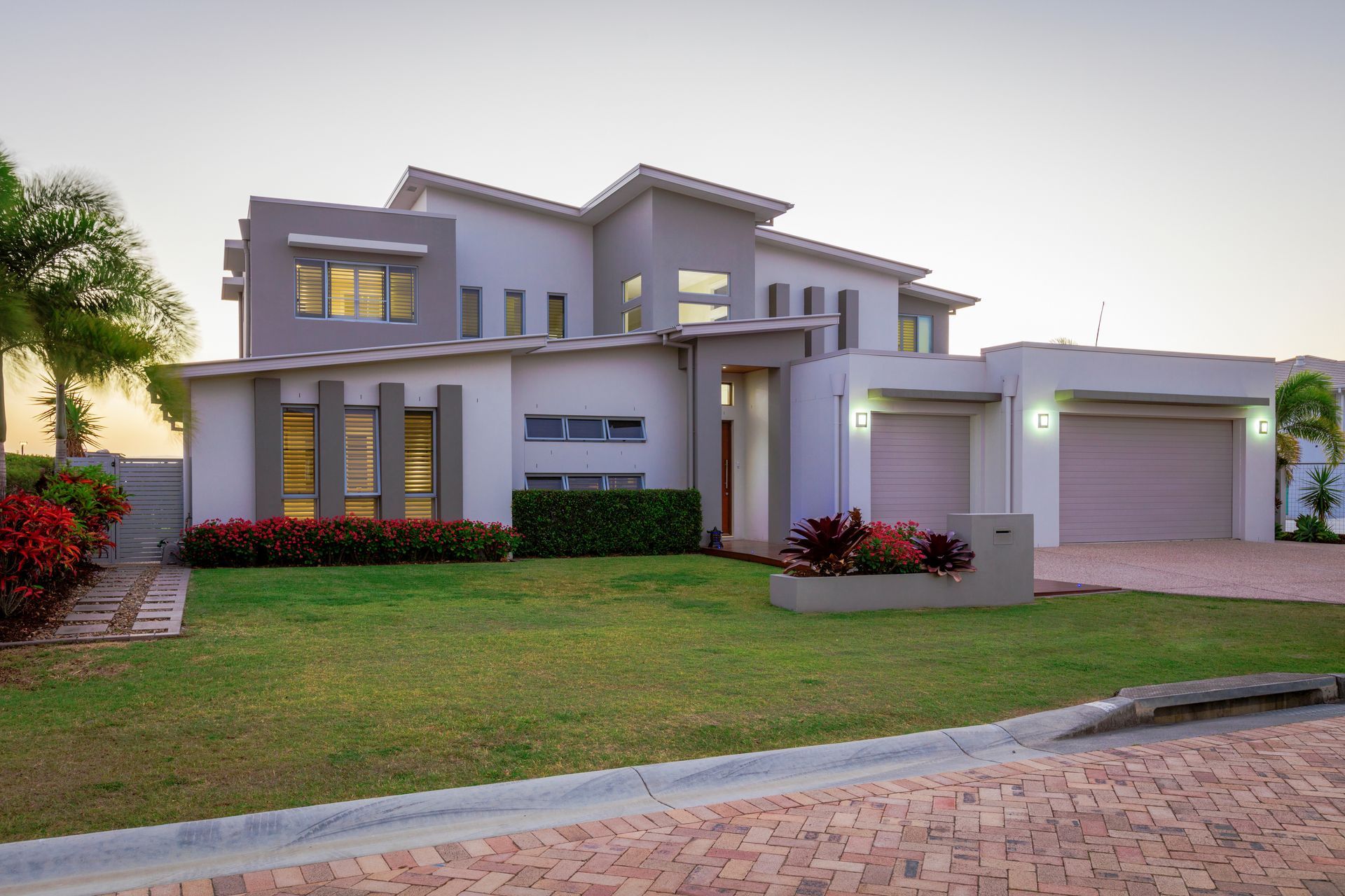 Modern two-story gray house with a front lawn, driveway, and attached garage at dusk