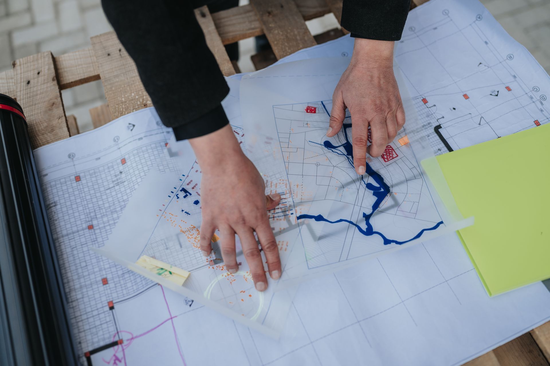 Hands marking a map with blue routes on a table, with a yellow sticky note nearby Hands marking a map with blue routes on a table, with a yellow sticky note nearby
