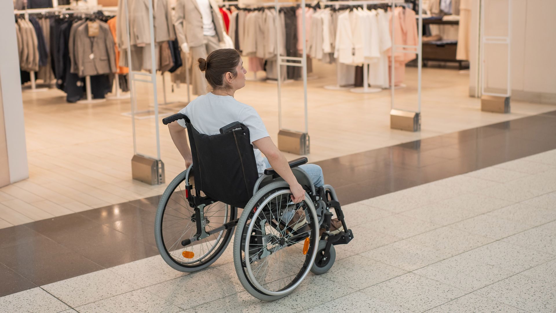 Person in a wheelchair facing a clothing store display in a mall