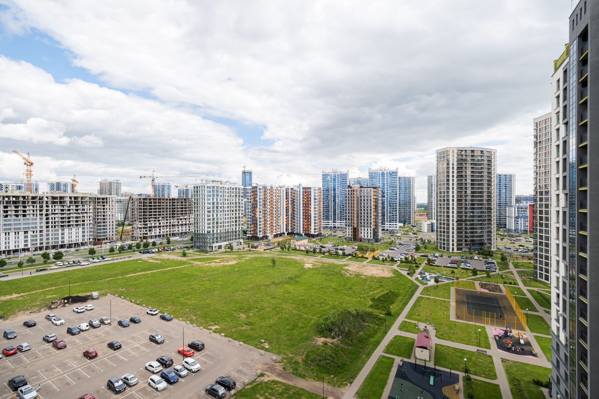 Wide view of modern apartment buildings a grassy courtyard and parking lot under cloudy sky Wide view of modern apartment buildings a grassy courtyard and parking lot under cloudy sky