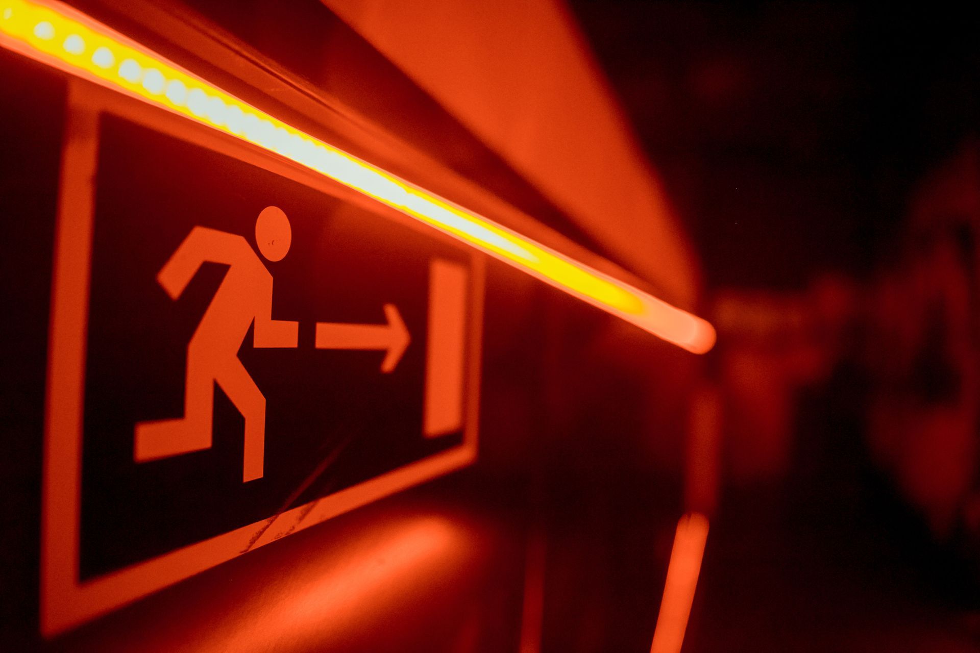Illuminated exit sign with a running figure and arrow glowing red in a dark hallway