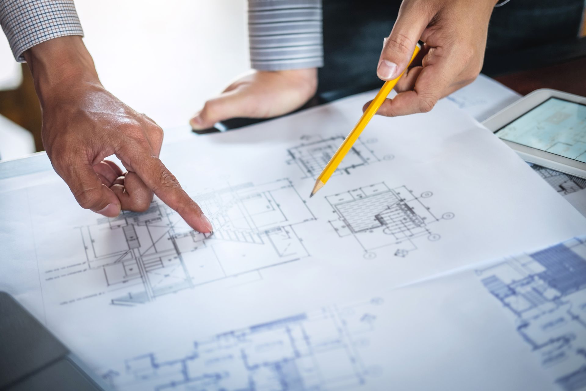 Hands and pencil pointing at architectural blueprints on a table