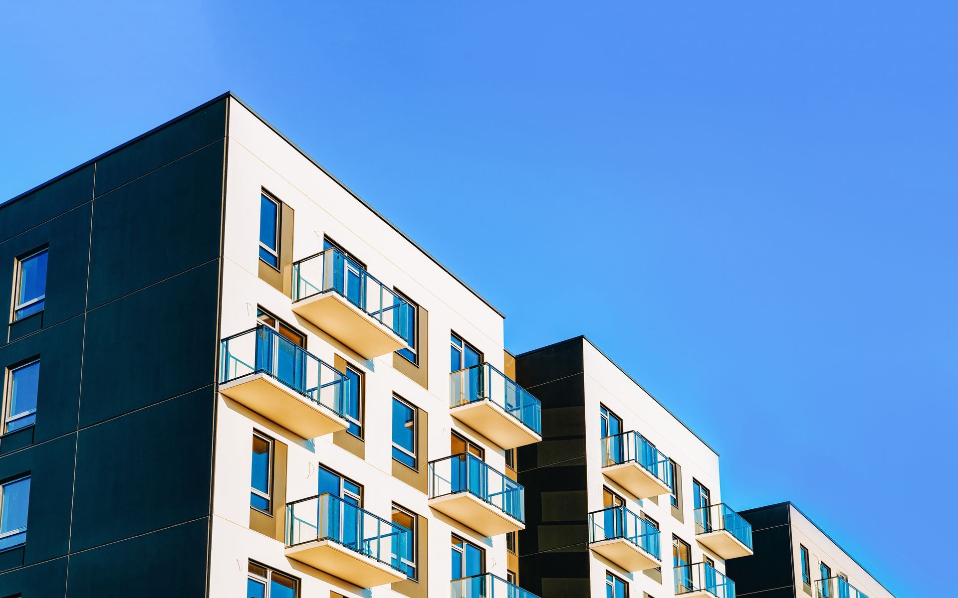 Modern apartment building with beige balconies against a clear blue sky Modern apartment building with beige balconies against a clear blue sky