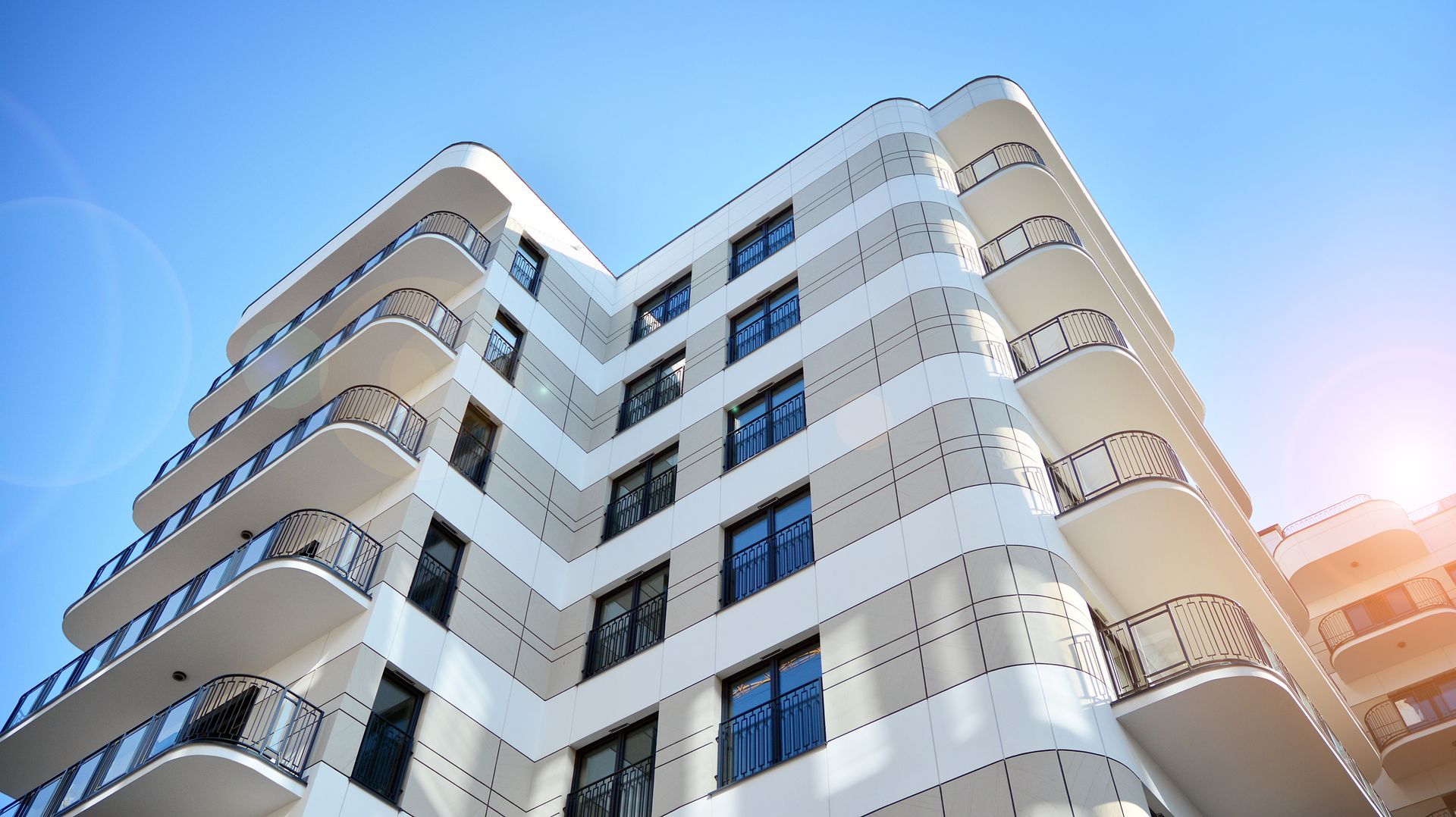 Modern white apartment building shot from below against a blue sky with sunlight glare Modern white apartment building shot from below against a blue sky with sunlight glare