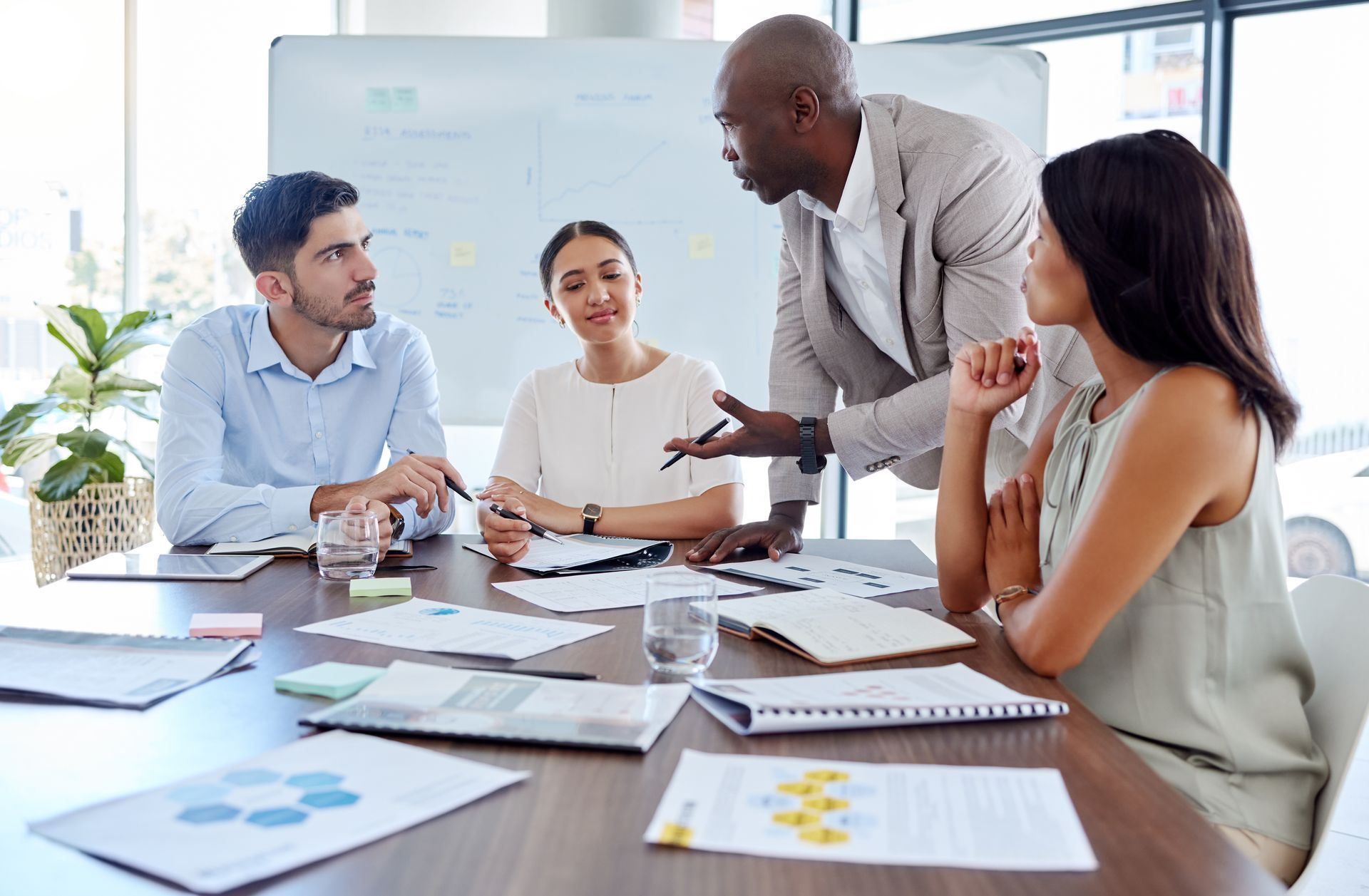 Business meeting with four people discussing documents around a conference table in a bright office