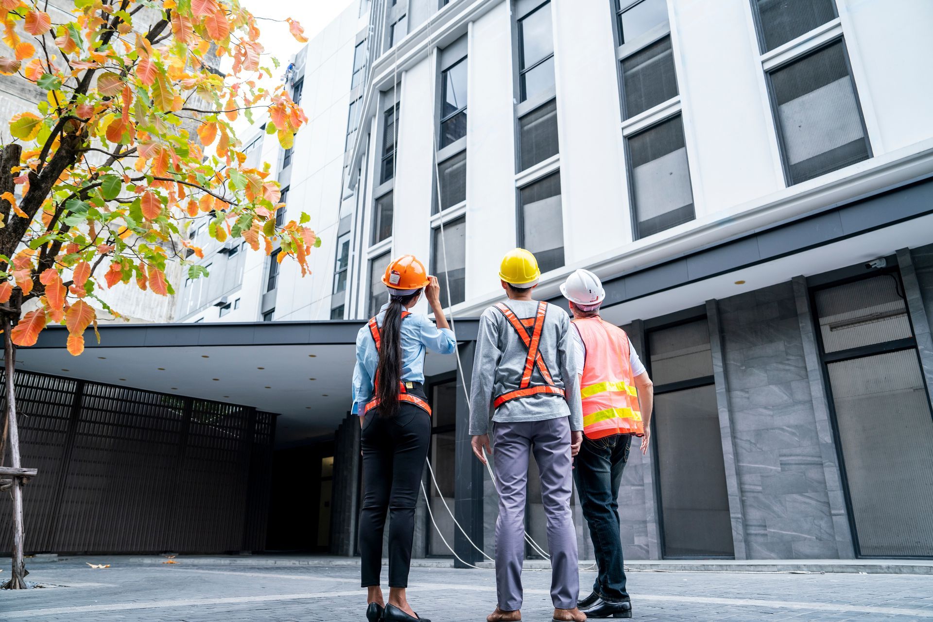 Three construction workers in hard hats inspect a modern building courtyard.