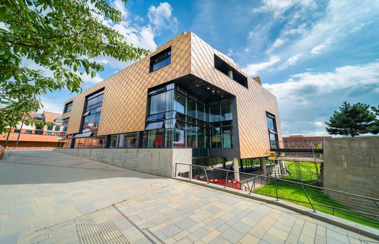 Modern brick-and-glass building with a paved courtyard and trees under a blue sky Modern brick-and-glass building with a paved courtyard and trees under a blue sky
