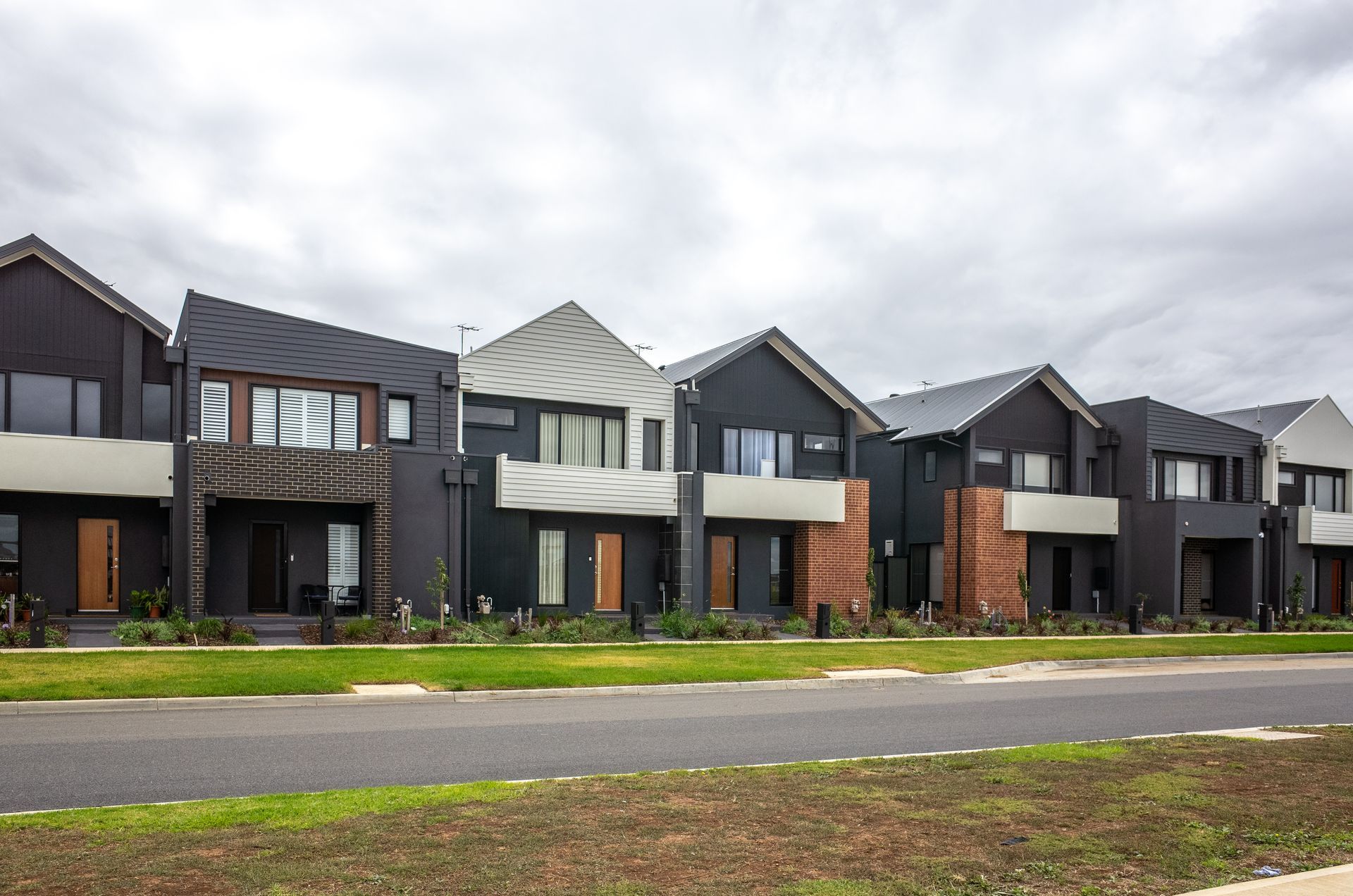 Row of modern two-story townhouses with dark gray and wood facades along a street.