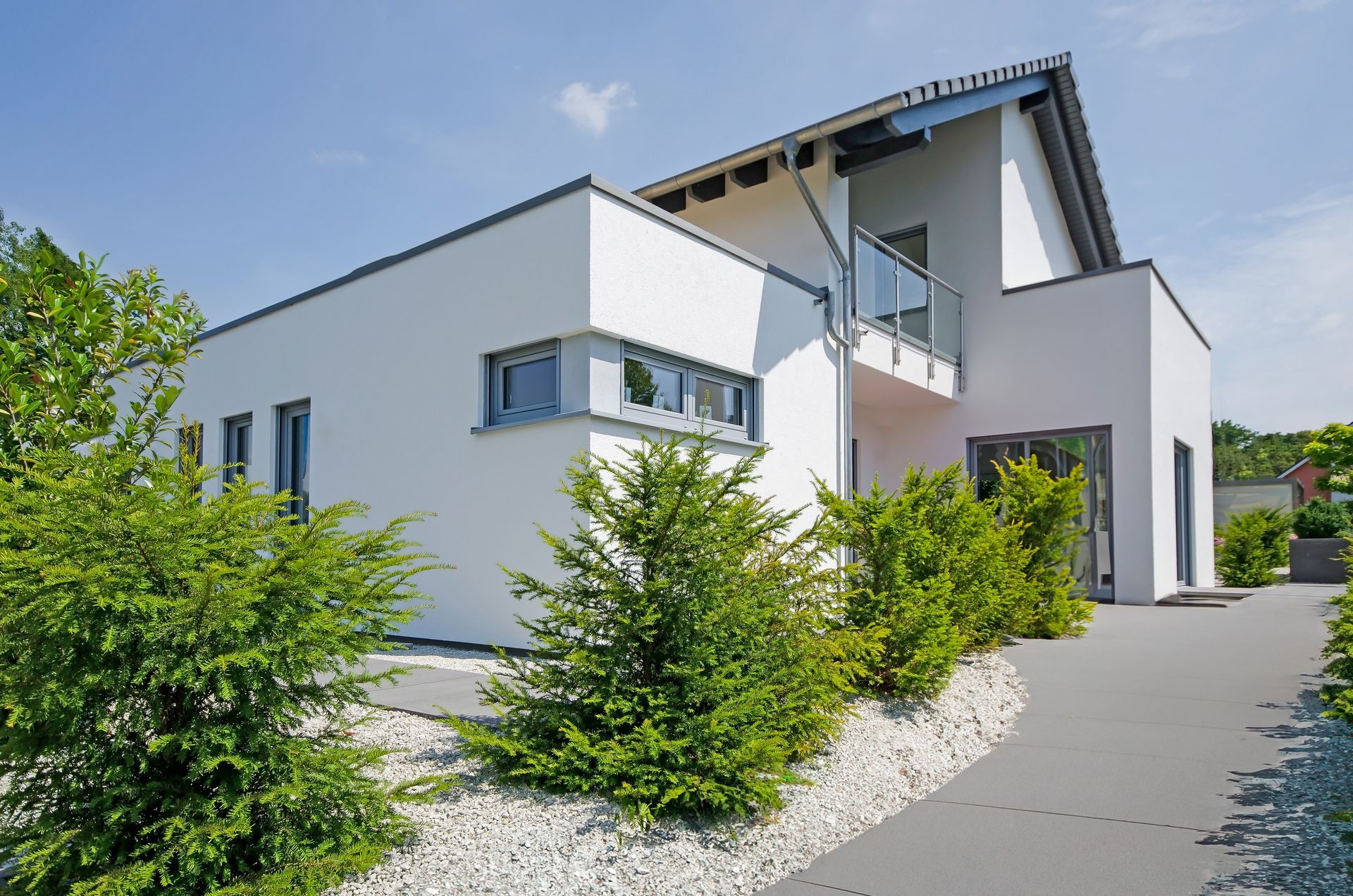 Modern white house with sloped roof, gravel landscaping, and a driveway beside green trees