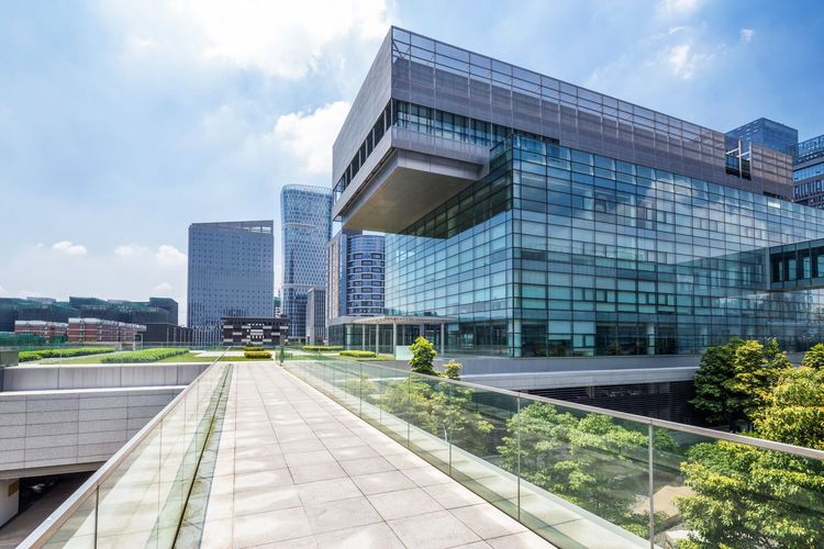 Modern glass office building with a wide stone walkway and blue sky Modern glass office building with a wide stone walkway and blue sky