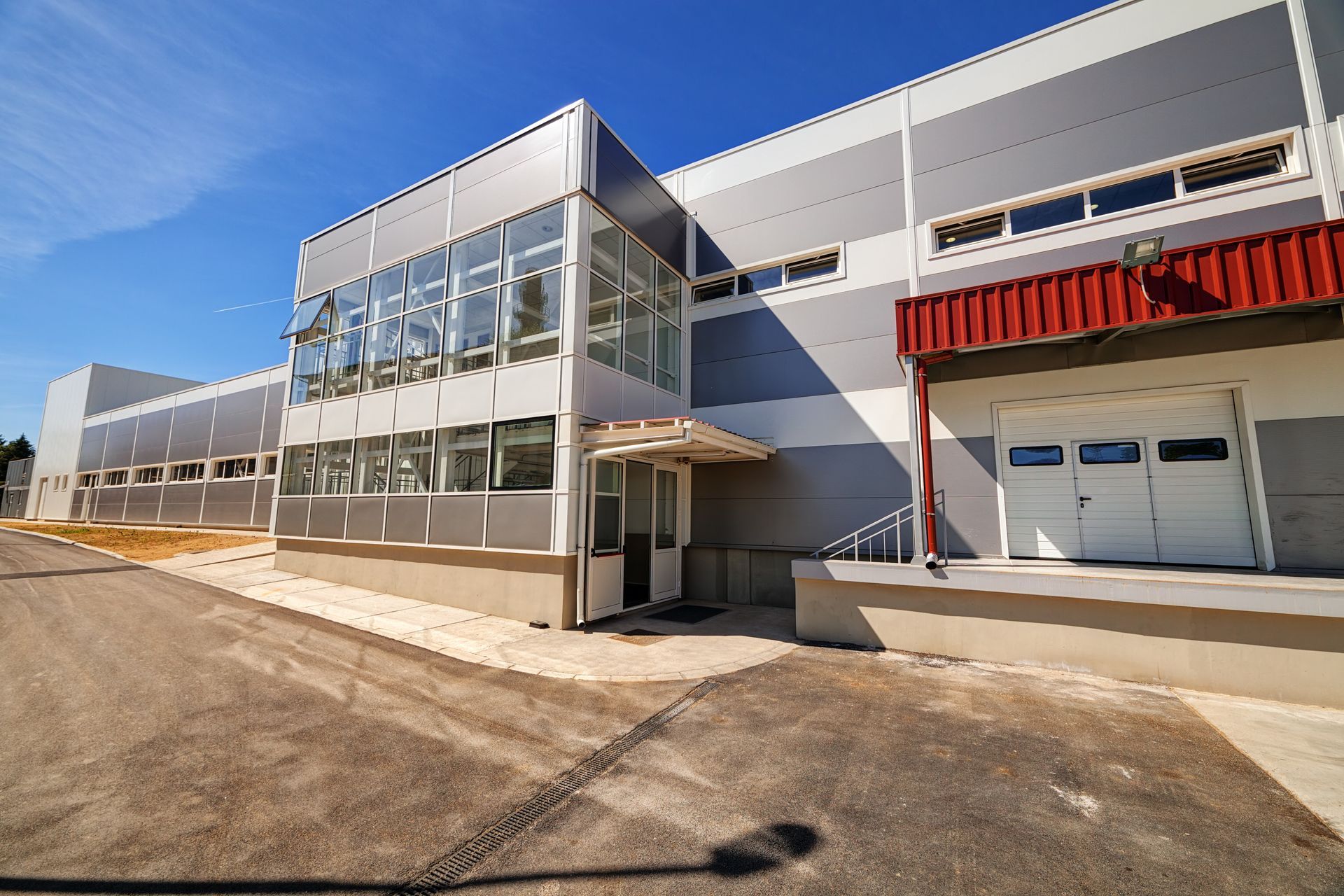 Modern industrial building with glass-fronted entrance, white facade, and red awning under a blue sky Modern industrial building with glass-fronted entrance, white facade, and red awning under a blue sky
