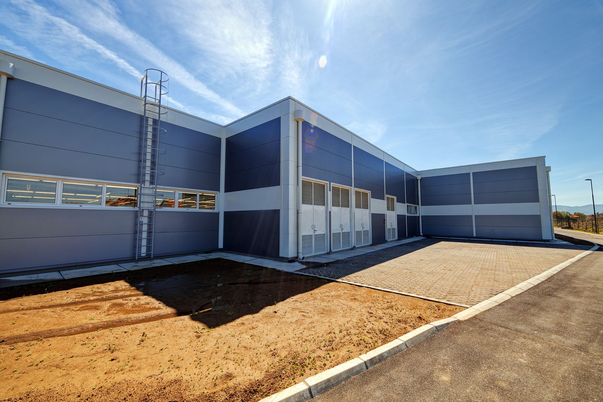 Modern blue-and-white modular building with windows and a dirt yard under a clear sky Modern blue-and-white modular building with windows and a dirt yard under a clear sky