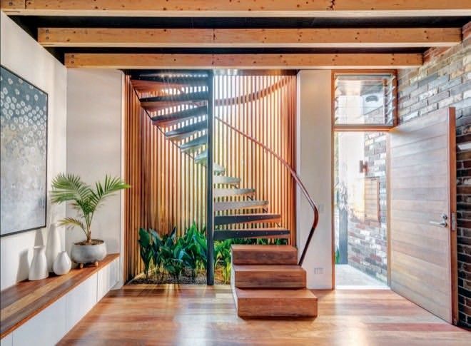 Modern staircase in a bright entryway with wood slat accents, plants, and a glass door. Modern staircase in a bright entryway with wood slat accents, plants, and a glass door.